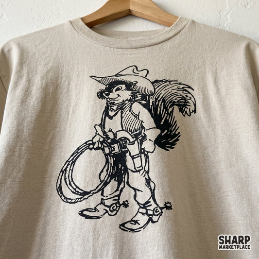 Detailed western squirrel illustration featuring a rodent in cowboy gear and a rope, printed in black on a neutral-colored t-shirt mockup.