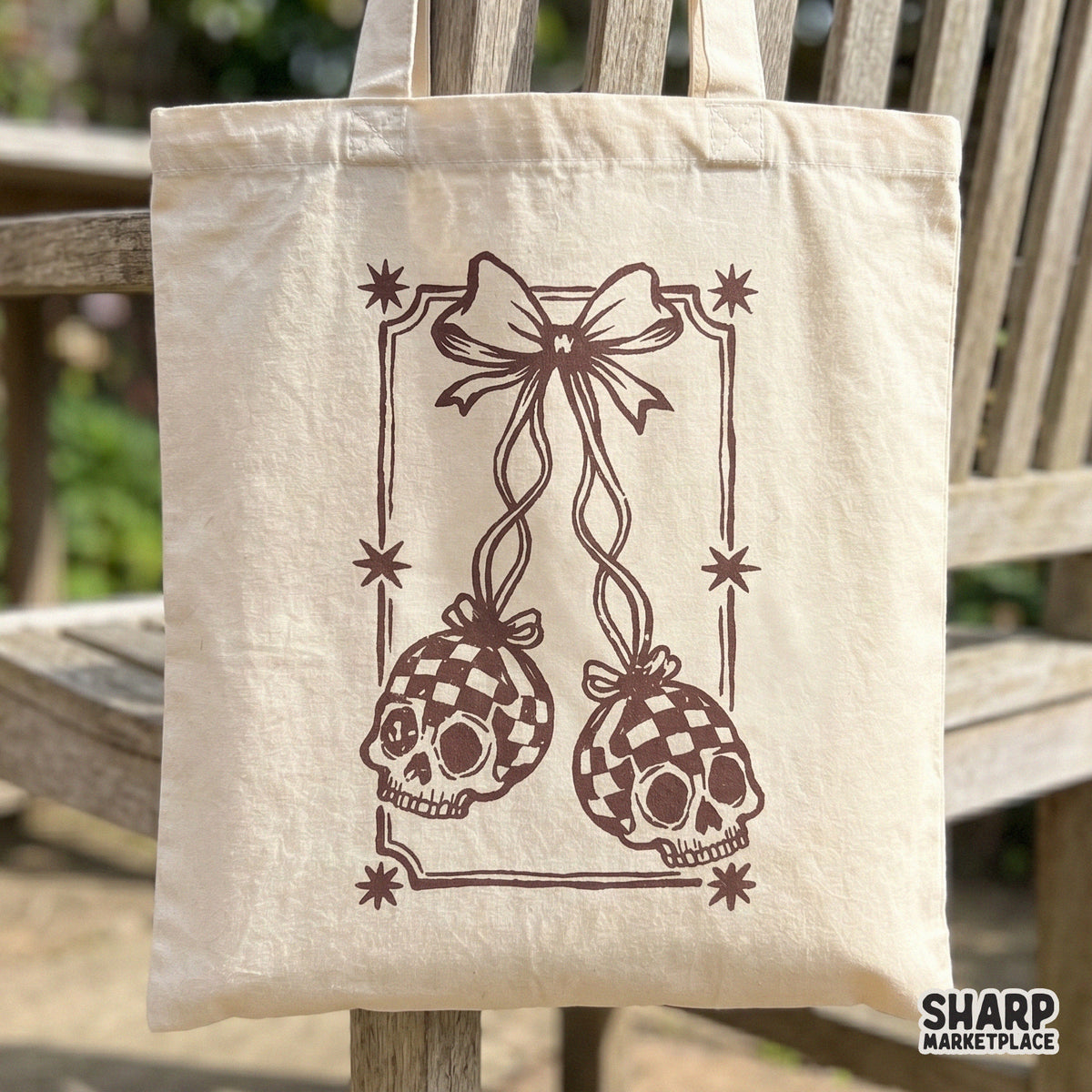 Spooky season sublimation design showing two hanging skull ornaments with a checkered pattern, tied with a bow and framed by stars in sepia tones.