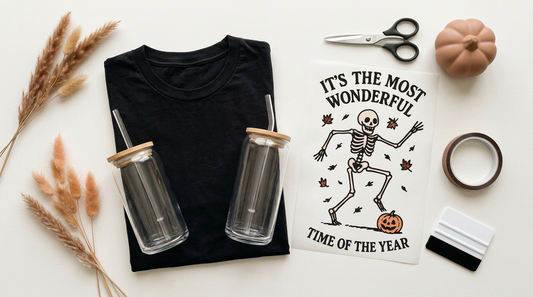 A flat lay mockup of a vintage black t-shirt and a glass can tumbler surrounded by crafting tools, ready for dancing skeleton