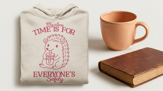 A cozy oversized hoodie folded next to a large ceramic coffee mug and a closed book on a light neutral background.