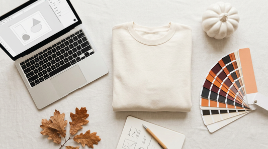 A cozy autumn workspace featuring blank apparel, a laptop, and seasonal props for print-on-demand planning.