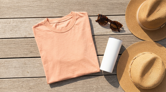 A flat lay of a blank oversized summer t-shirt next to a sublimation tumbler, sunglasses, and a beach hat on a wooden deck.