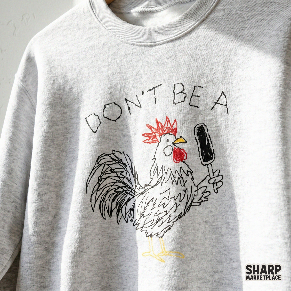 Trendy chicken shirt design featuring a hand-drawn rooster with a hairbrush and the quote Don't Be A, shown on a heather gray sweatshirt.