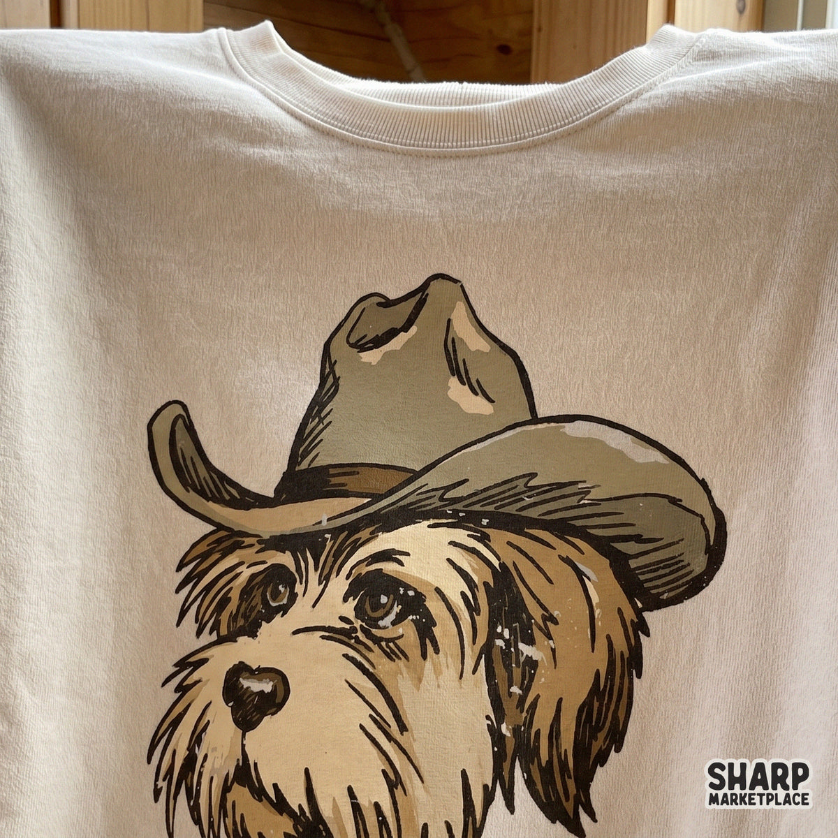 Digital design of a charming scruffy ranch dog in a western hat, showcased as a screen-printed graphic on a cream-colored t-shirt for trendy apparel.