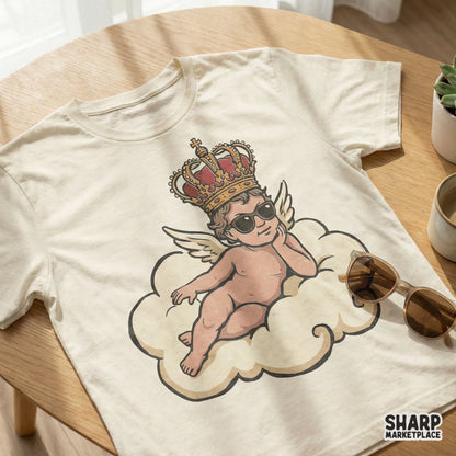 Digital design of a sassy winged baby angel with sunglasses and a crown, displayed on a cream colored t-shirt mockup.