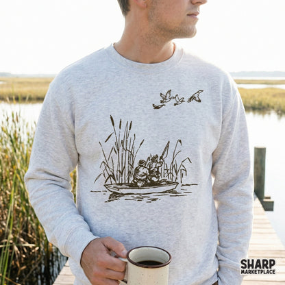 A rustic monochromatic duck hunting scene featuring hunters in a small boat, displayed as a digital design on a light gray crewneck sweatshirt.