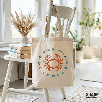 Digital design of a hand-drawn orange crab surrounded by a nautical ring of teal shells and starfish, displayed on a canvas tote bag mockup.