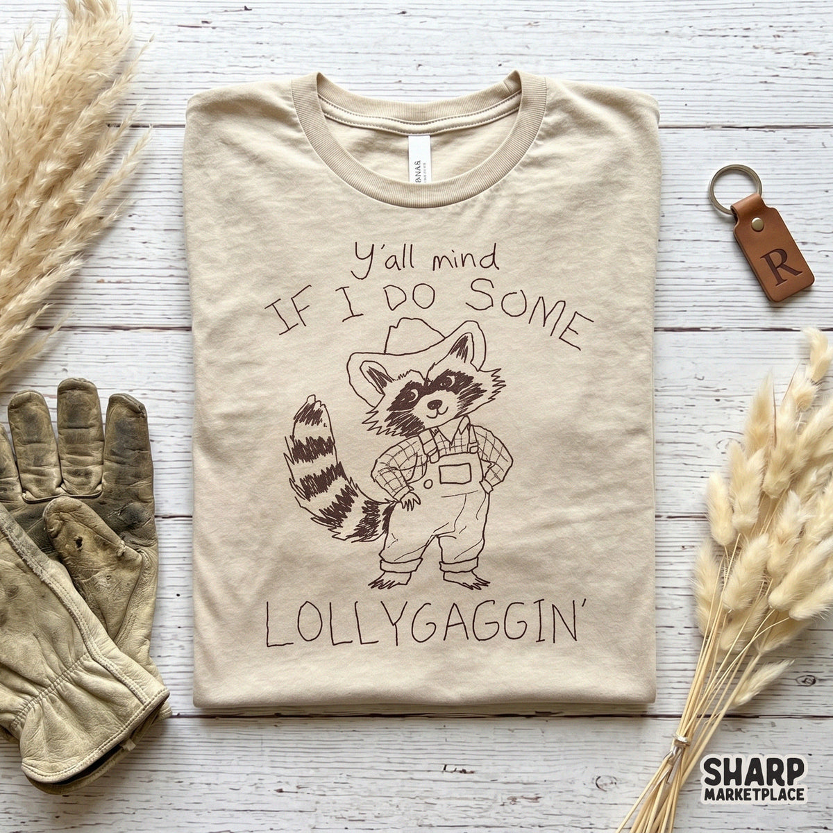 Charcoal line art of a cute raccoon character in country attire with the phrase Y'all Mind If I Do Some Lollygaggin' for printable wall art.