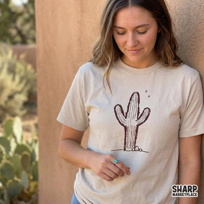 A hand-drawn saguaro cactus graphic printed on a beige t-shirt, showcasing a vintage western aesthetic perfect for boho apparel and sublimation.
