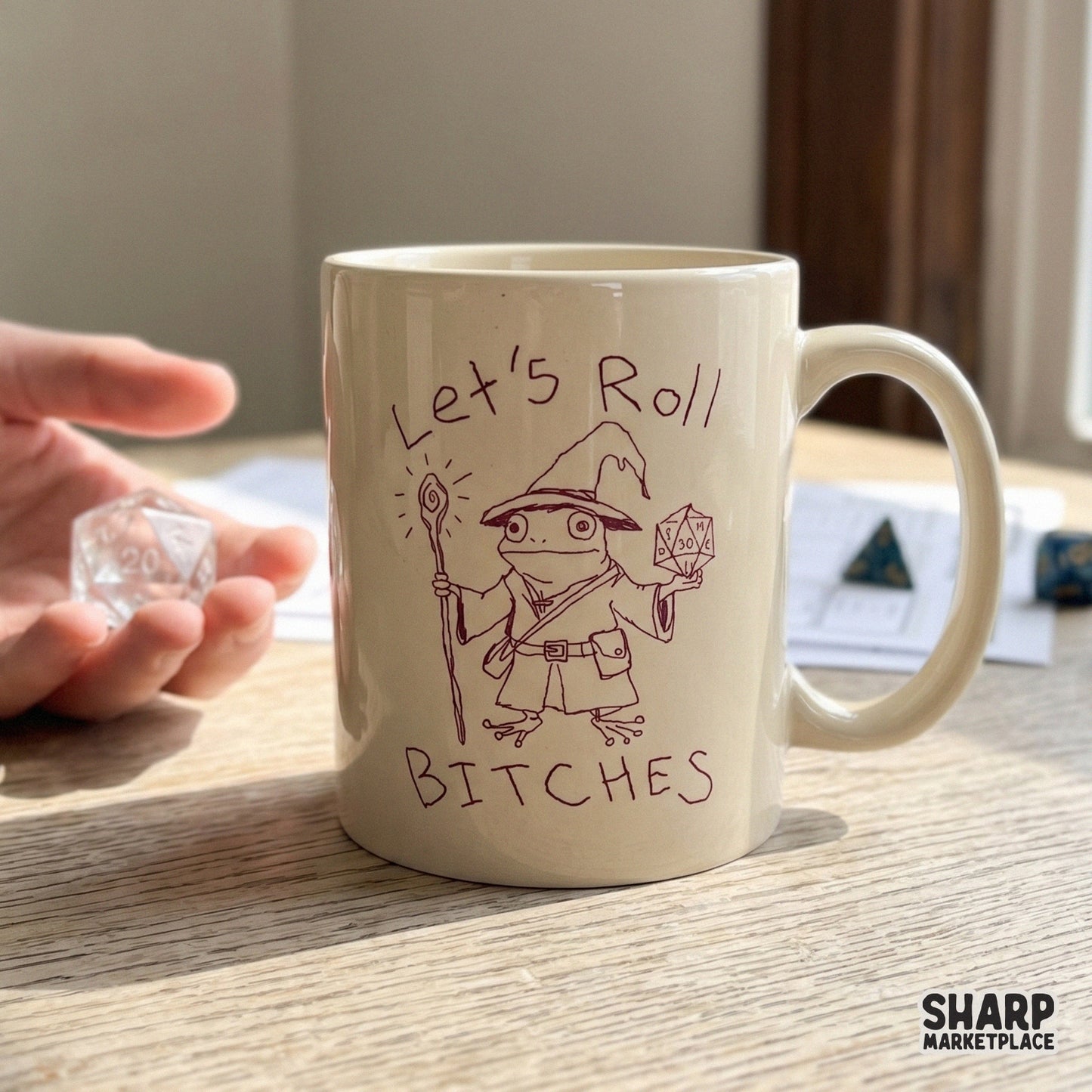 A ceramic mug featuring a whimsical maroon line art design of a magic toad wizard holding a gaming die with the sarcastic text Let's Roll Bitches.
