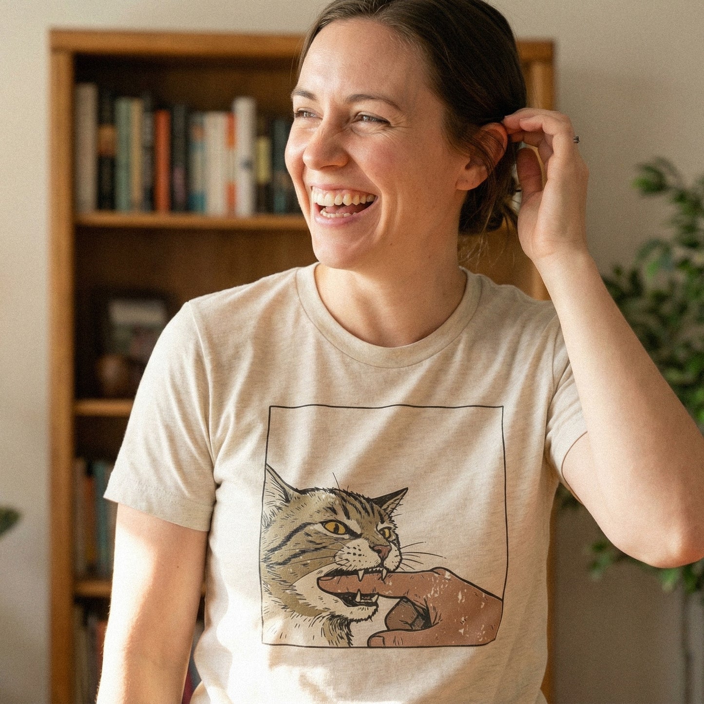 Funny cat biting finger digital design shown on a t-shirt, featuring a feisty tabby cat illustration with expressive yellow eyes and comic book aesthetics.