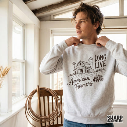 A light-colored sweatshirt featuring a printed design of a farm barn, vintage tractor, and the quote Long Live American Farmers.