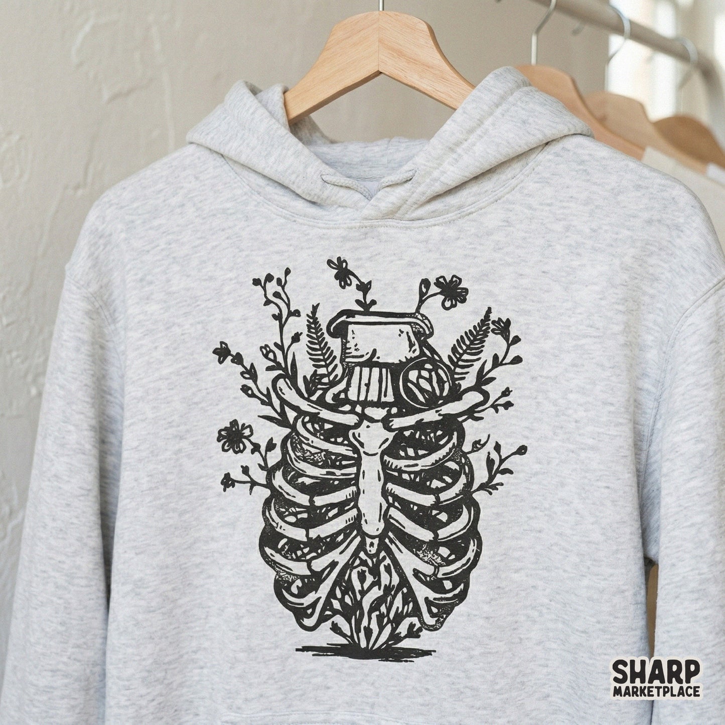 Black and white floral rib cage digital art printed on a heather gray hoodie, showcasing a botanical anatomy style for trendy clothing.