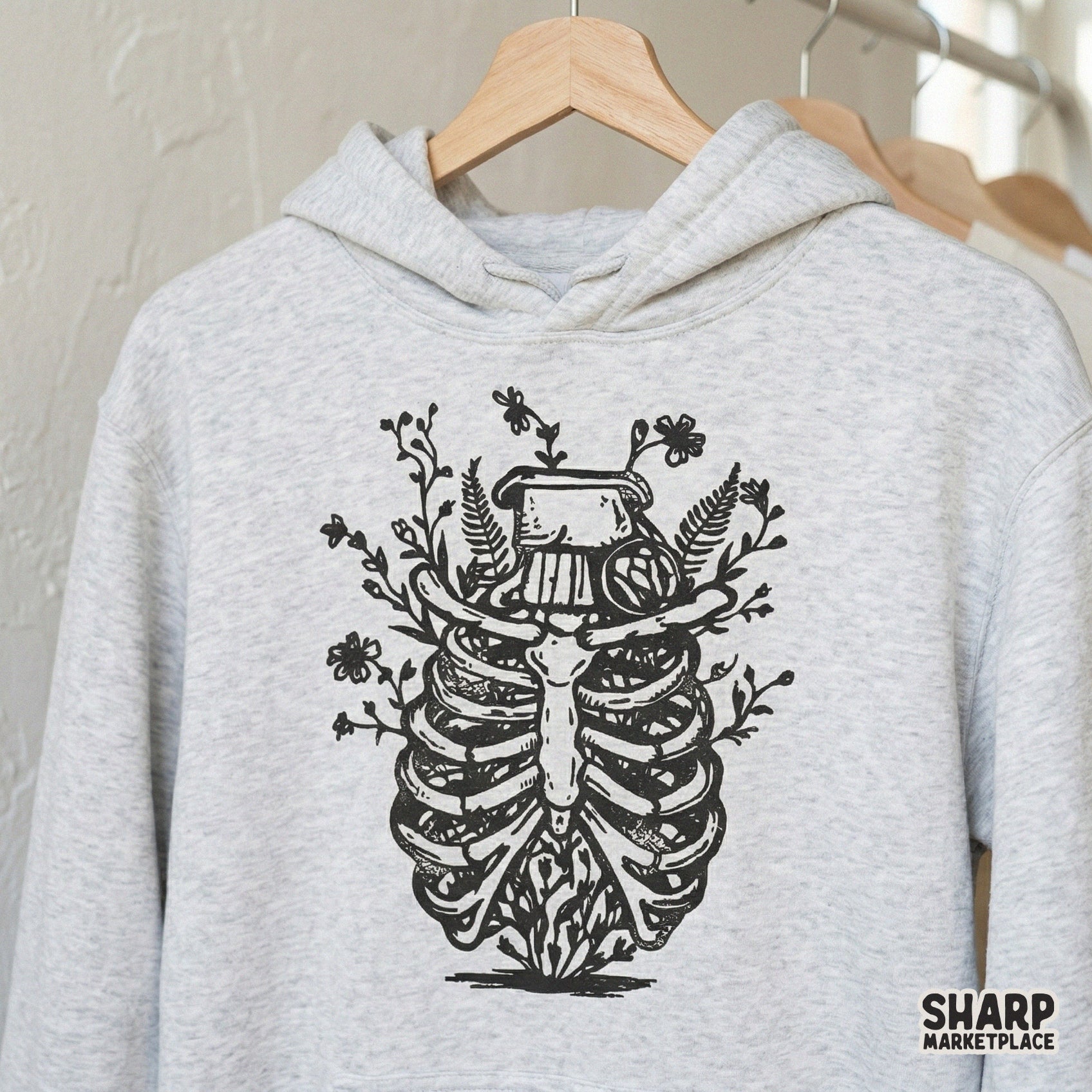 Black and white floral rib cage digital art printed on a heather gray hoodie, showcasing a botanical anatomy style for trendy clothing.