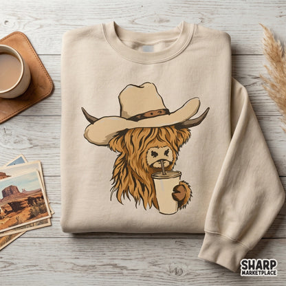 Trendy western sublimation design featuring a fuzzy highland cow in a cowboy hat drinking from a coffee cup, displayed on a neutral-colored sweatshirt.