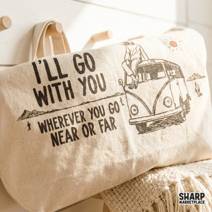 Distressed vintage road trip graphic printed on a canvas tote bag, showing a van in a desert landscape with mountains, cacti, and a warm sun.