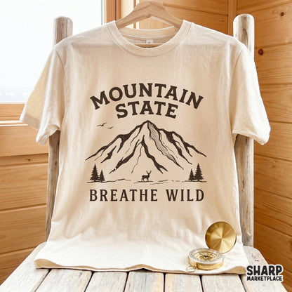 Distressed brown mountain landscape graphic with a deer and pine trees on a cream t-shirt mockup, perfect for outdoor apparel and DIY projects.