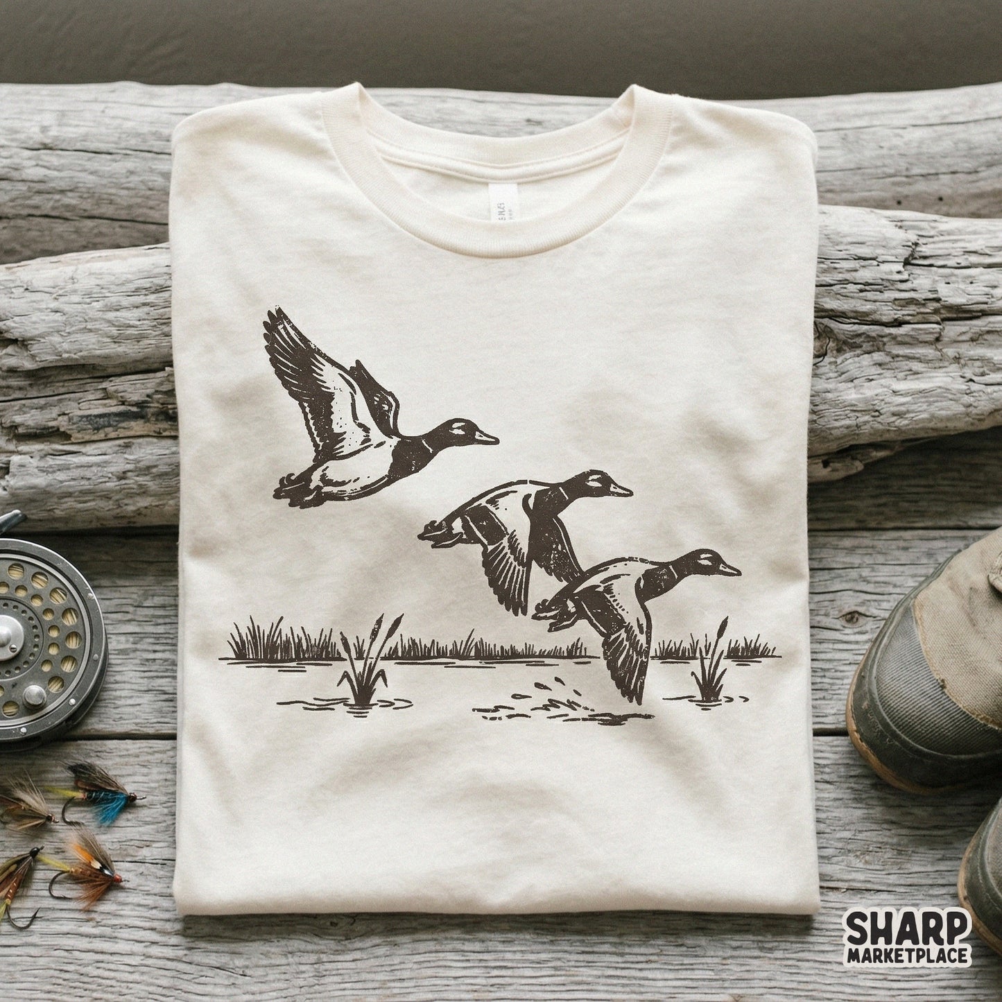 Rustic black and white duck trio design printed on a neutral-colored t-shirt, featuring a detailed hand-drawn style for outdoor-themed apparel.
