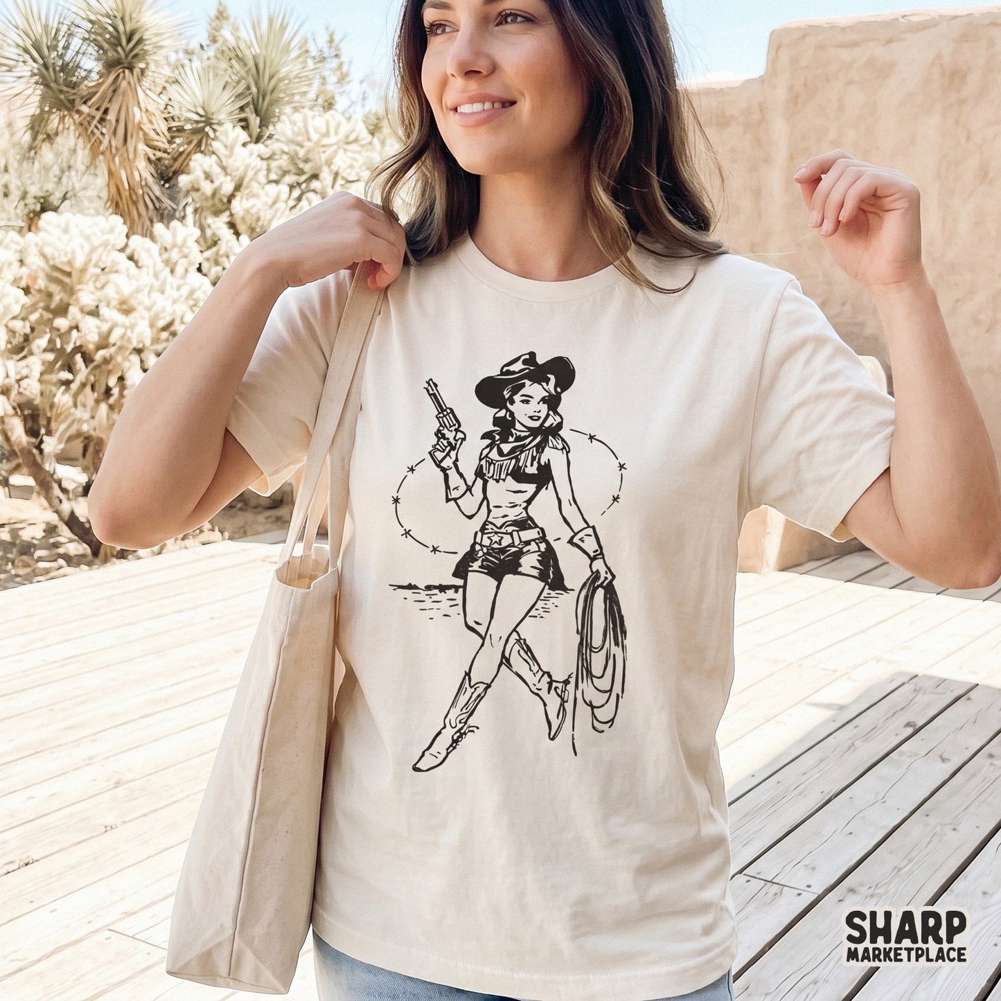 Vintage western cowgirl graphic with a revolver and rope, displayed as a black ink design on a cream colored t-shirt for trendy rodeo inspired apparel.