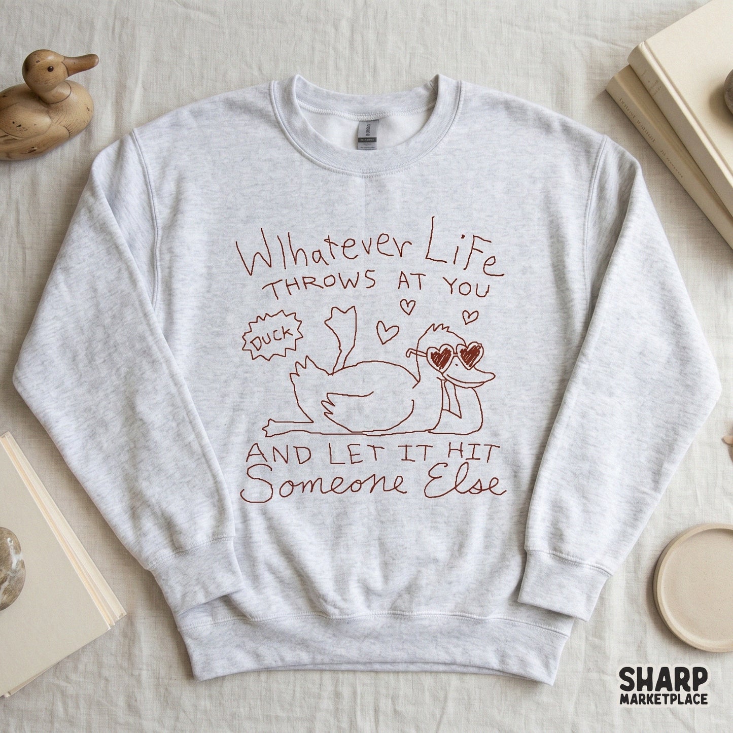 Playful digital illustration of a duck lounging with feet up, heart icons, and the witty quote Whatever Life Throws At You And Let It Hit Someone Else.