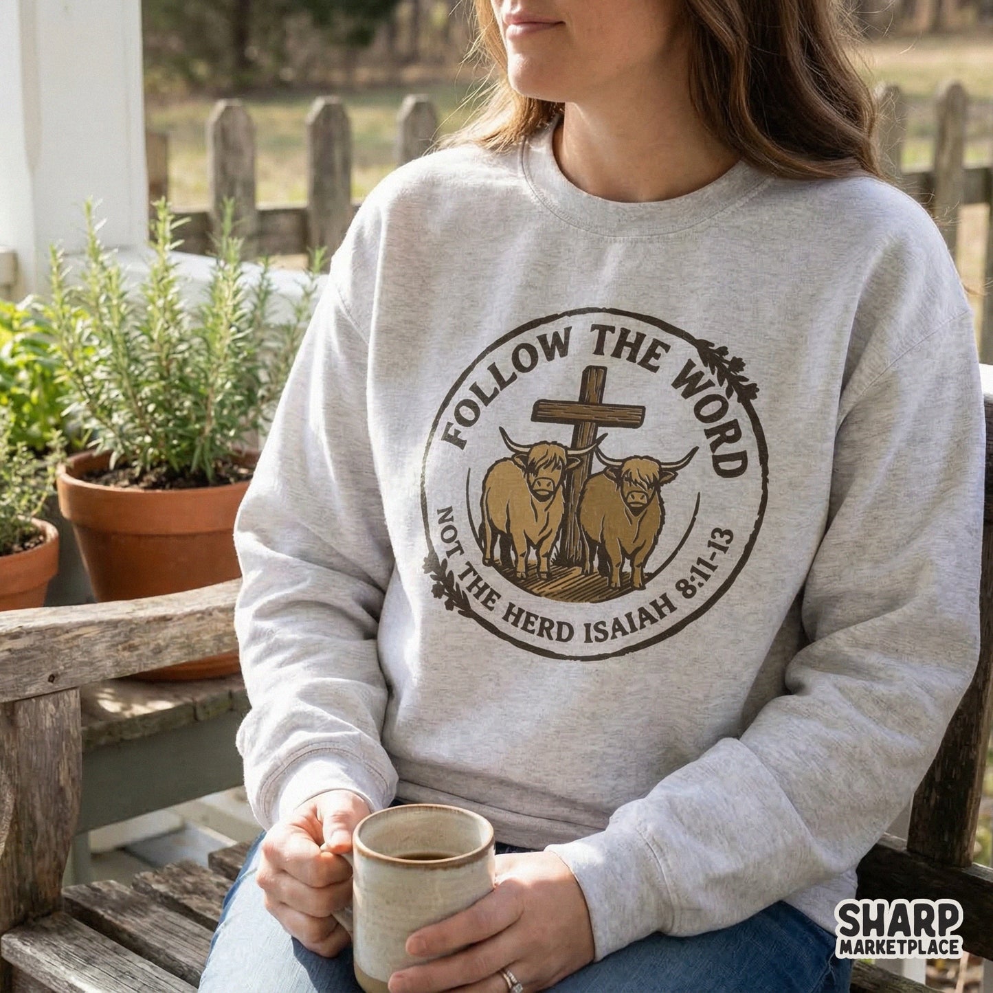 Western style Christian design on a light gray sweatshirt, showing two highland cows and a wooden cross with the quote Follow The Word Not The Herd.
