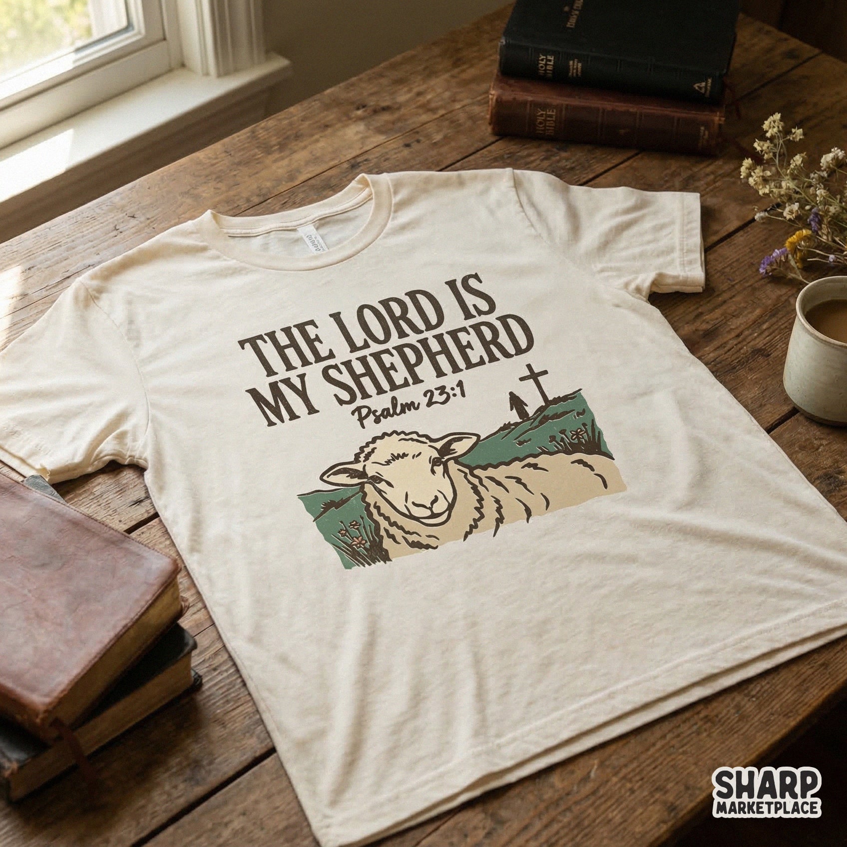 Cream colored t-shirt mockup displaying a rustic Bible verse design with a hand-drawn sheep illustration and a distant cross on a hill.