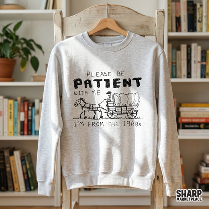 Light gray sweatshirt mockup displaying a funny black ink sketch of a horse-drawn wagon with the quote Please Be Patient With Me I'm From The 1900s.