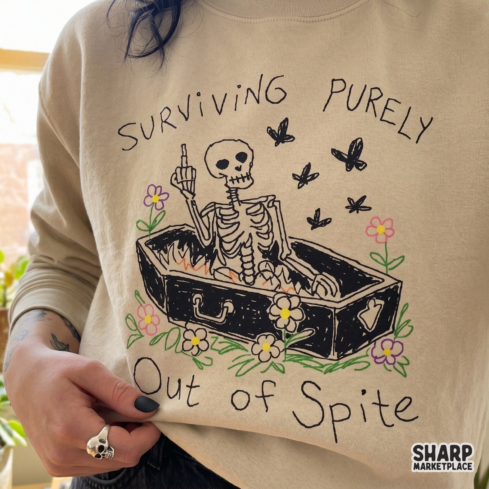 Digital sublimation design of a skeleton in a coffin with flowers and butterflies, featuring the sarcastic quote Surviving Purely Out Of Spite for shirts.