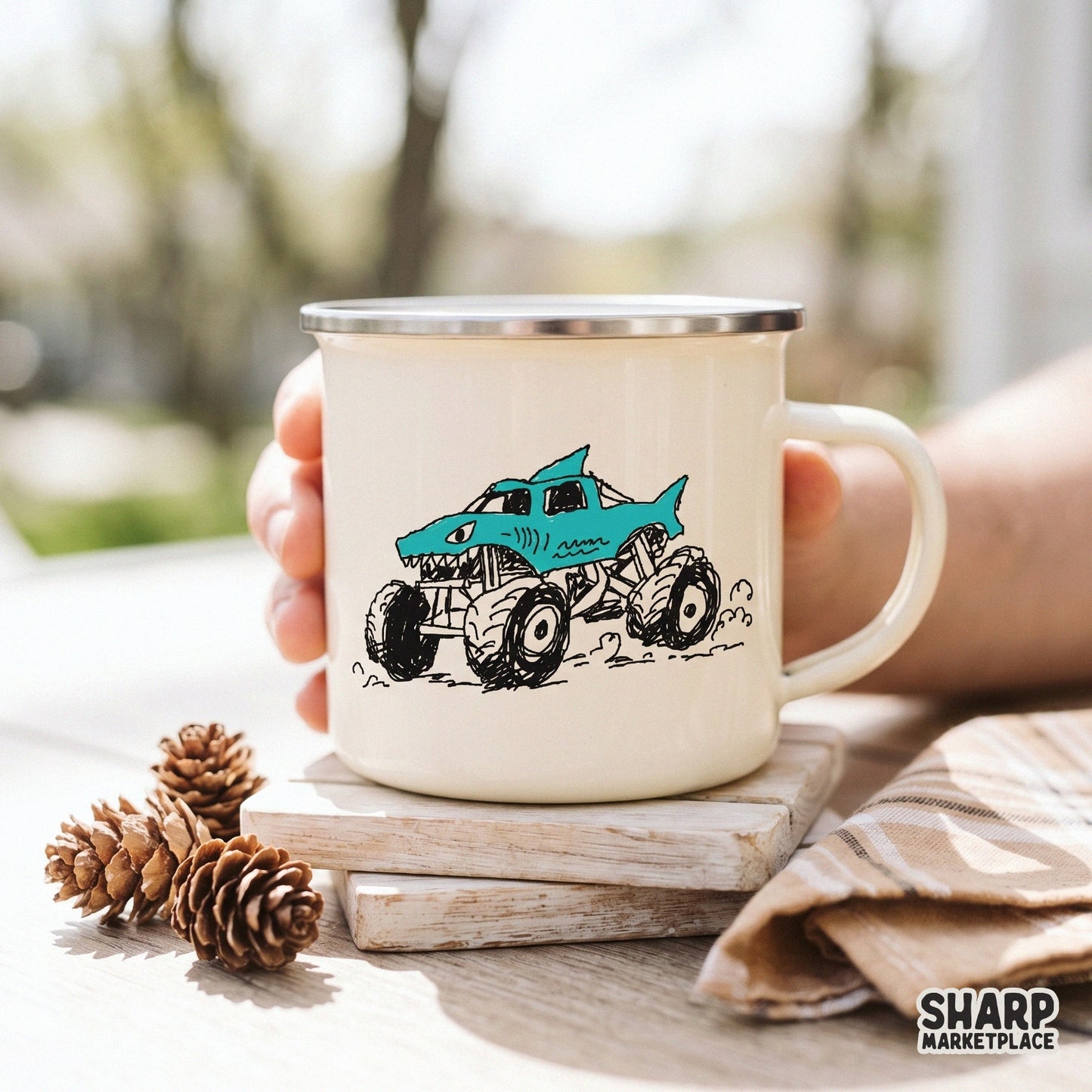 Cyan blue shark-themed monster truck graphic with rugged tires and sharp teeth, displayed on a cream-colored enamel mug for DIY print projects.