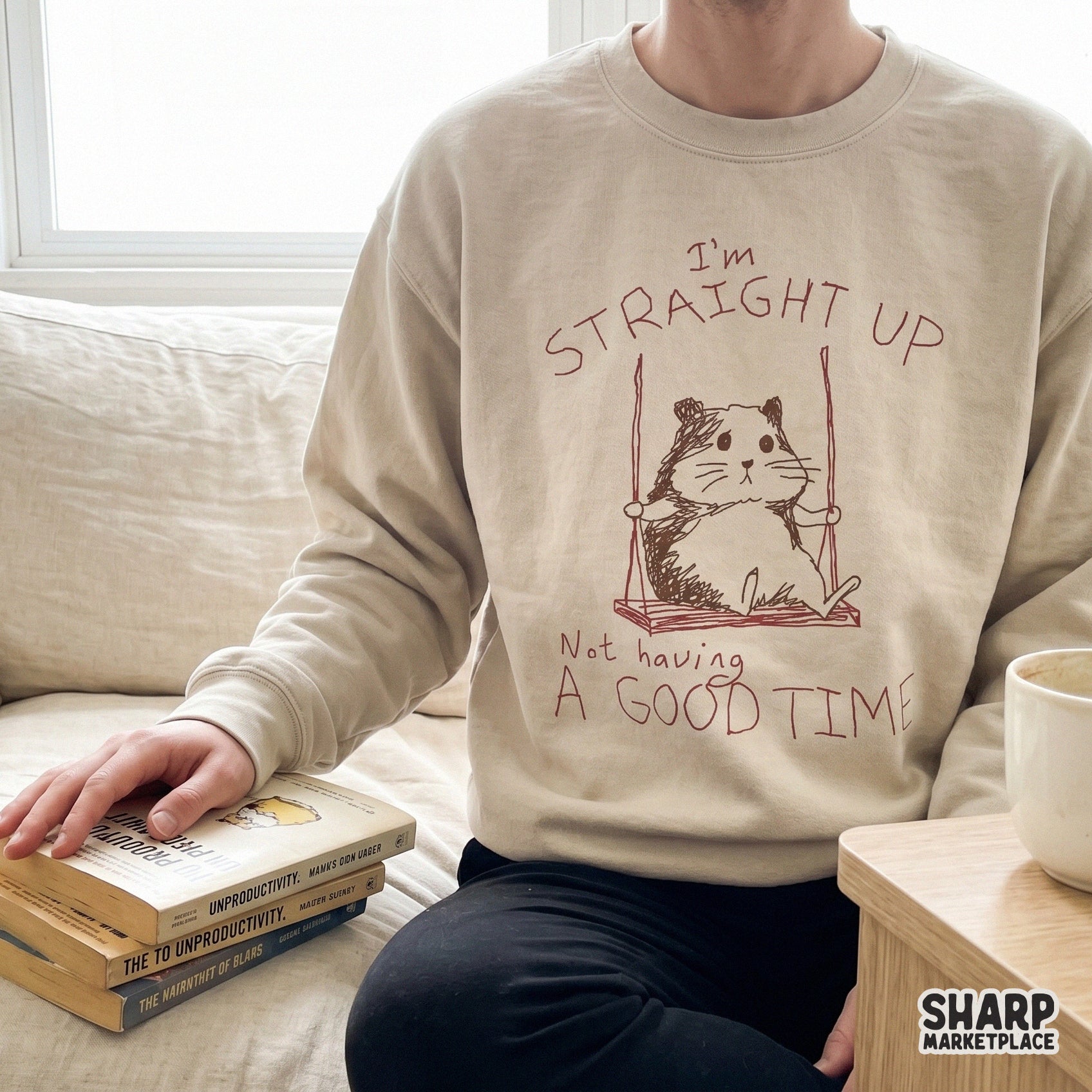 A beige sweatshirt featuring a minimalist sketch of a sad hamster on a swing with sarcastic handwritten text, perfect for custom apparel and DIY projects.