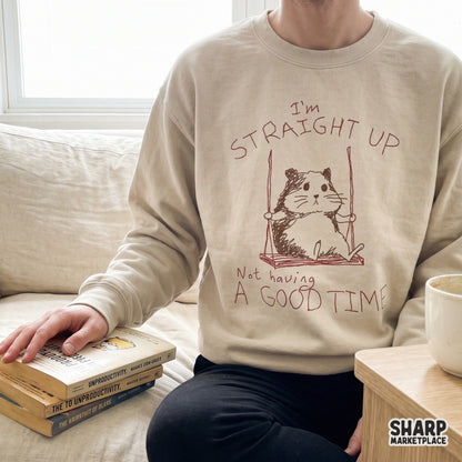 A beige sweatshirt featuring a minimalist sketch of a sad hamster on a swing with sarcastic handwritten text, perfect for custom apparel and DIY projects.