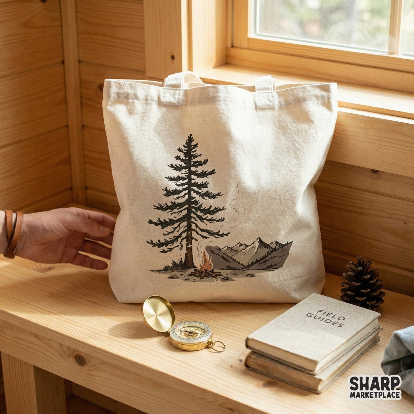 Digital camping illustration on a white tote bag showing a pine tree and campfire against mountain peaks, perfect for outdoor apparel sublimation.
