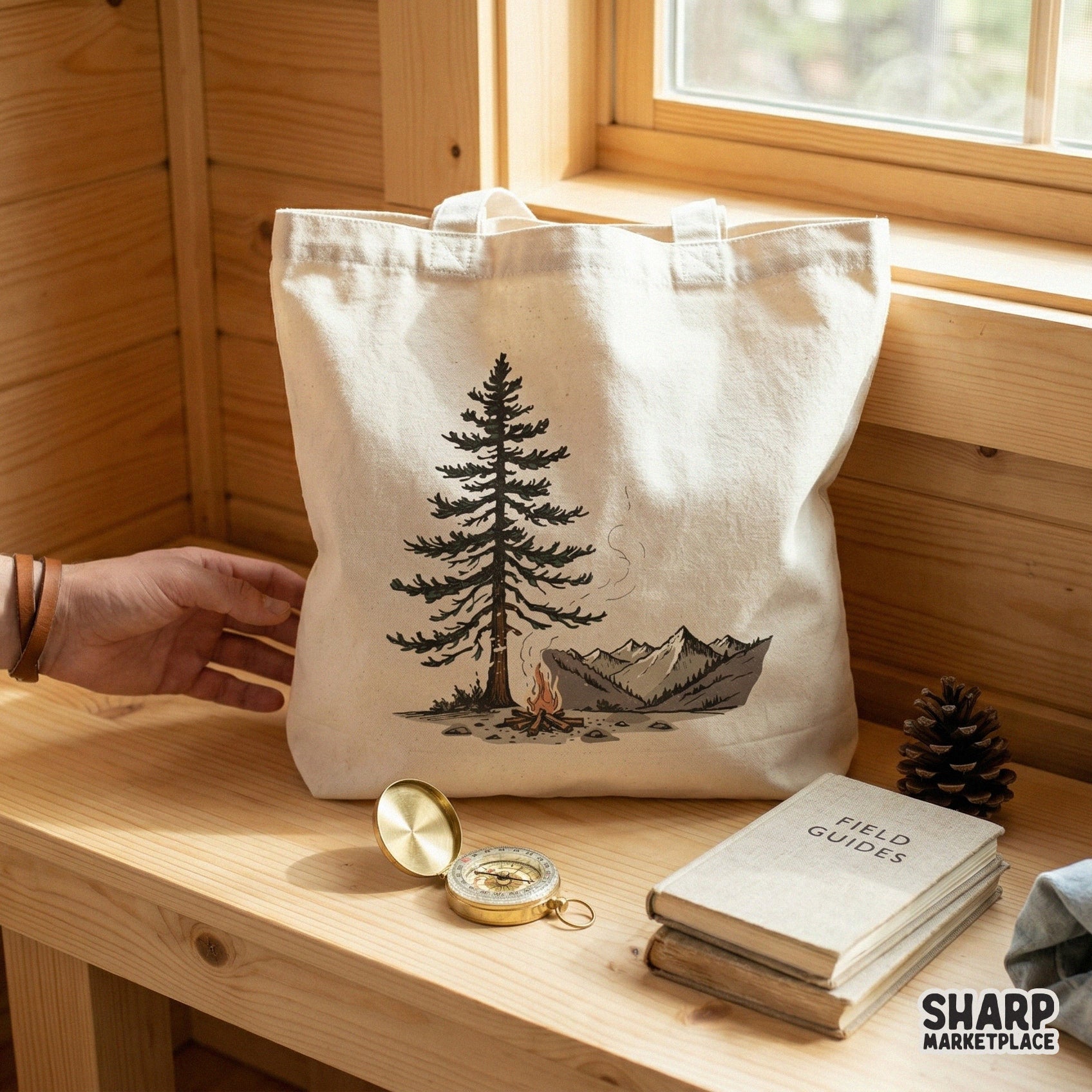 Digital camping illustration on a white tote bag showing a pine tree and campfire against mountain peaks, perfect for outdoor apparel sublimation.
