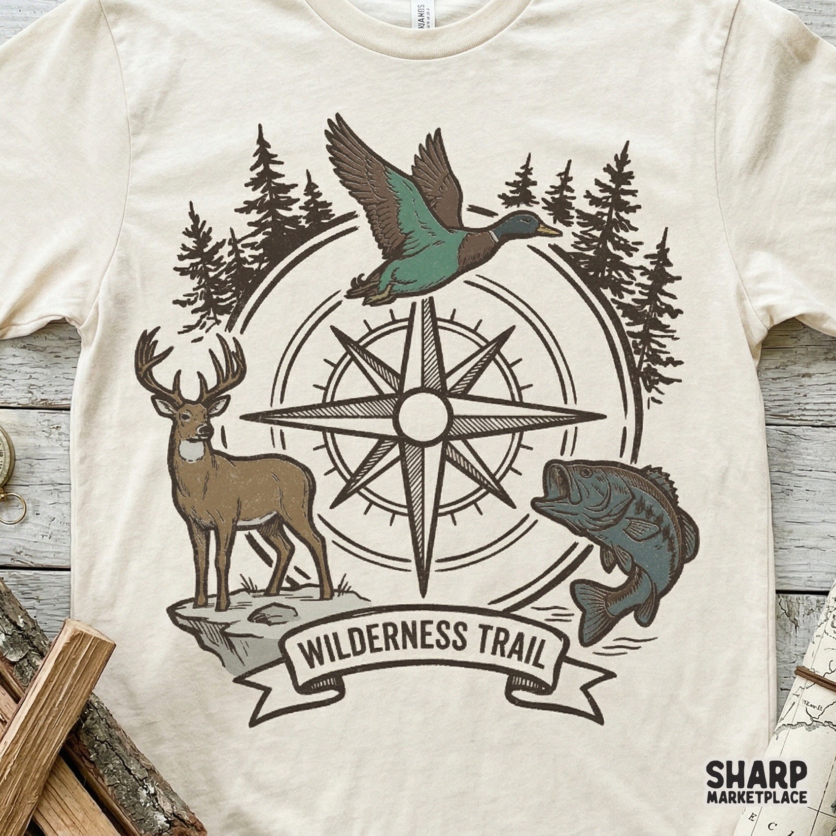 Vintage-style hunting and fishing graphic on a cream t-shirt, showcasing a compass rose, deer, duck, and bass with the text Wilderness Trail.