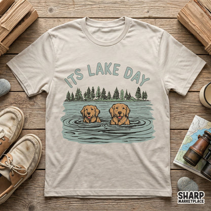 T-shirt mockup showcasing a hand-drawn illustration of two swimming golden retrievers under pine trees with the text It's Lake Day for summer projects.