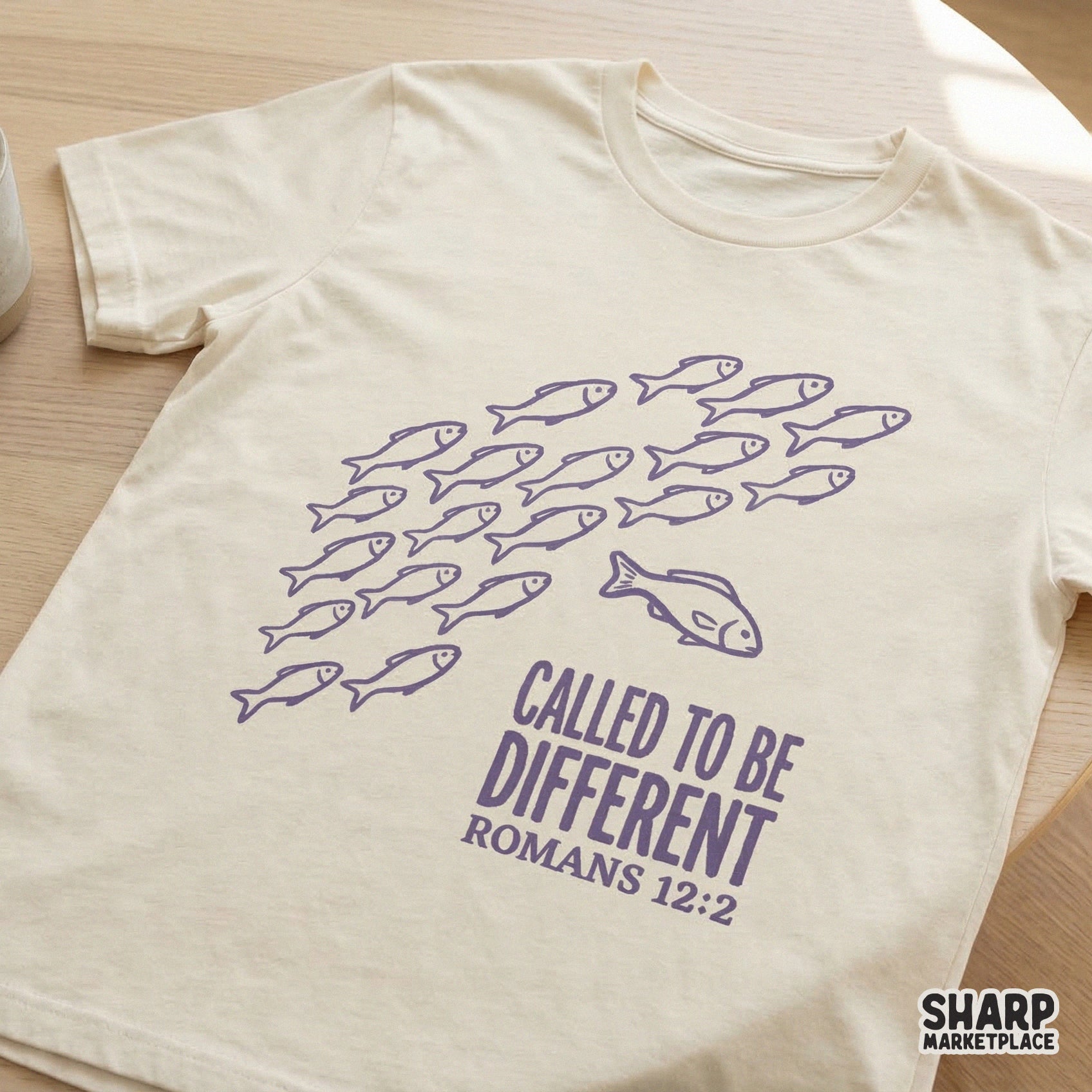 Christian faith design on a cream t-shirt showing a school of purple fish and one fish swimming against the current with the quote Called To Be Different.