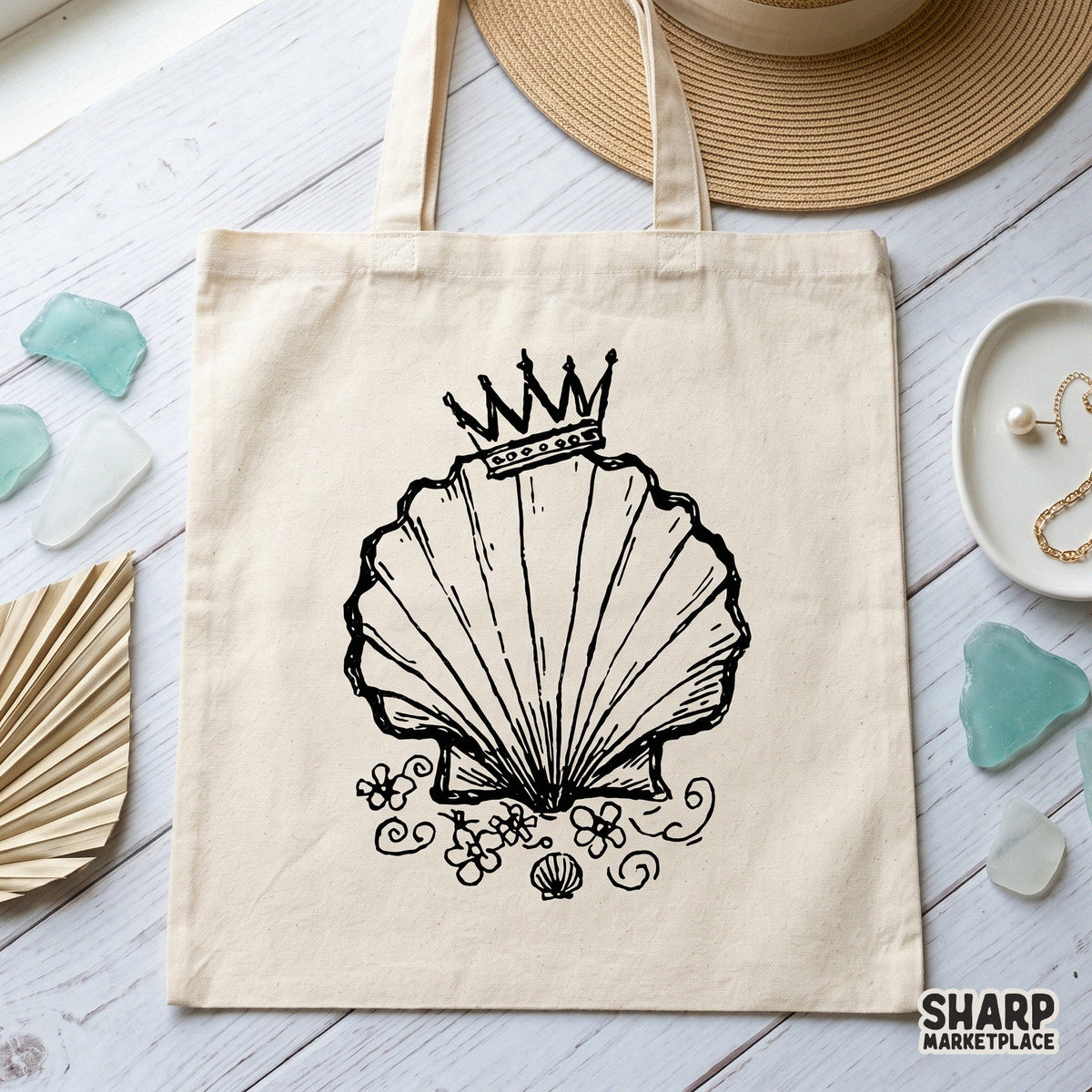 Black and white sketch of a crowned seashell with floral accents, displayed on a canvas tote bag for a trendy coastal apparel or DIY craft project.