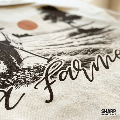 Retro farm field graphic with a worker, sunset, and hand-lettered a farmer text, ideal for fall-themed apparel and sublimation projects.