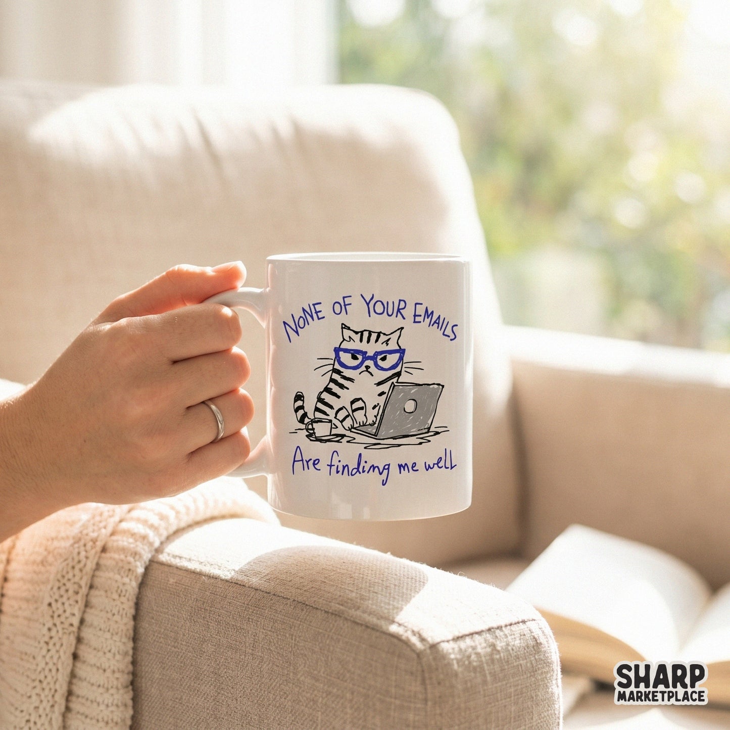 A white coffee mug featuring a grumpy tabby cat in blue glasses working on a laptop with the sarcastic quote None Of Your Emails Are Finding Me Well.