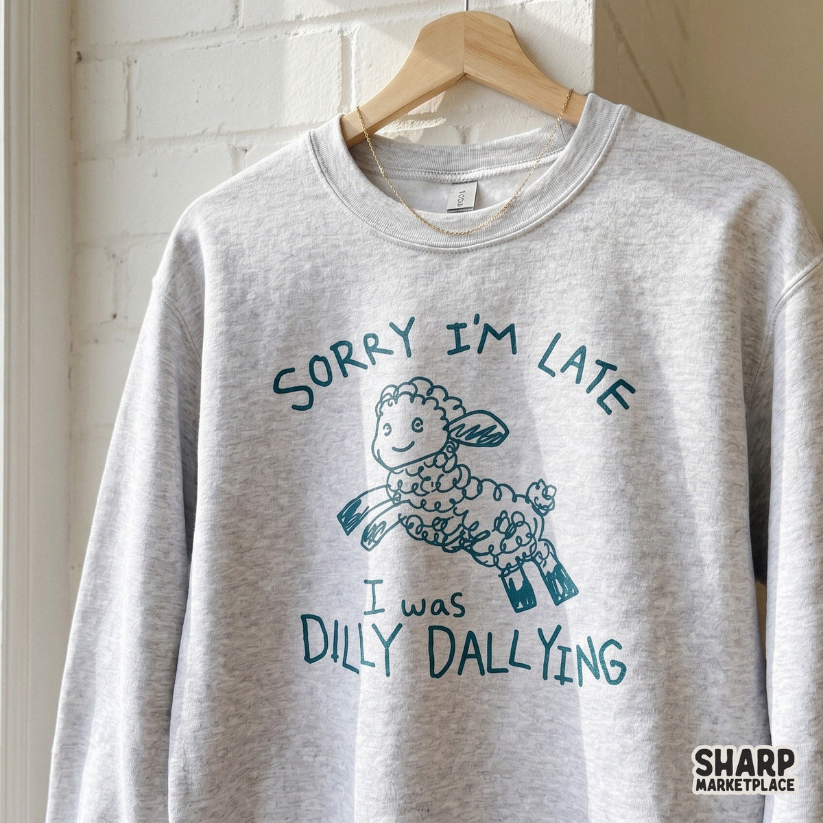 A heather gray sweatshirt featuring a whimsical teal sketch of a jumping sheep and the funny quote Sorry I'm Late I Was Dilly Dallying.