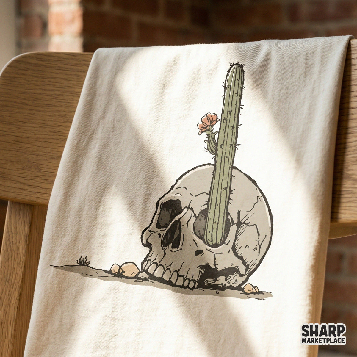 Vintage-style illustration of a human skull with a cactus and flower, displayed on a cream-colored fabric surface for apparel and sublimation.