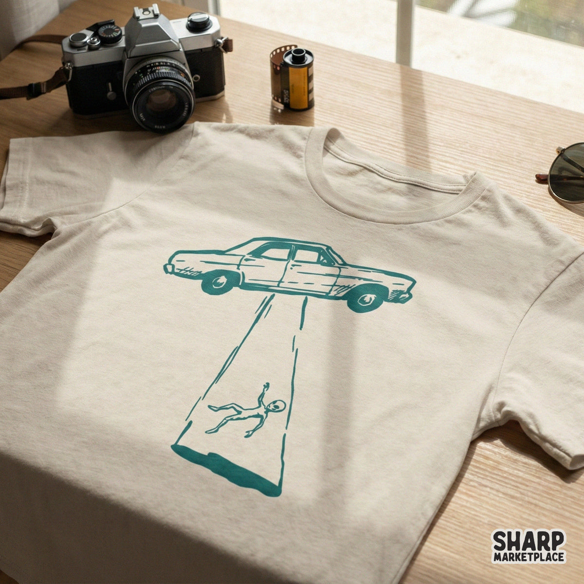 Retro sci-fi digital design featuring a car caught in an alien tractor beam, printed in teal on a light-colored t-shirt mockup for DIY projects.