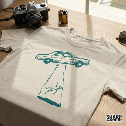 Retro sci-fi digital design featuring a car caught in an alien tractor beam, printed in teal on a light-colored t-shirt mockup for DIY projects.