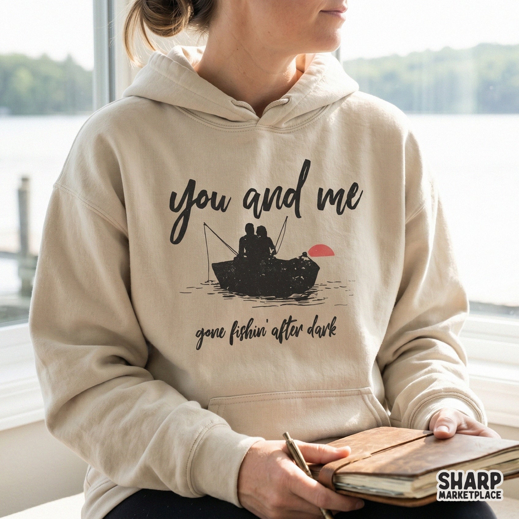Distressed vintage-style graphic showing a couple fishing in a rowboat at sunset, printed on a neutral-colored hoodie for a romantic outdoor look.