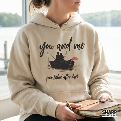 Distressed vintage-style graphic showing a couple fishing in a rowboat at sunset, printed on a neutral-colored hoodie for a romantic outdoor look.