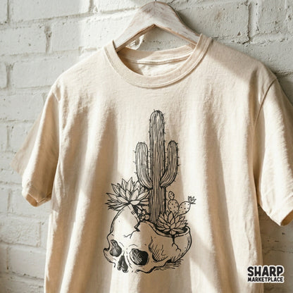 Trendy boho desert skull design featuring a saguaro cactus and succulents, shown as a black graphic printed on a neutral colored t-shirt.
