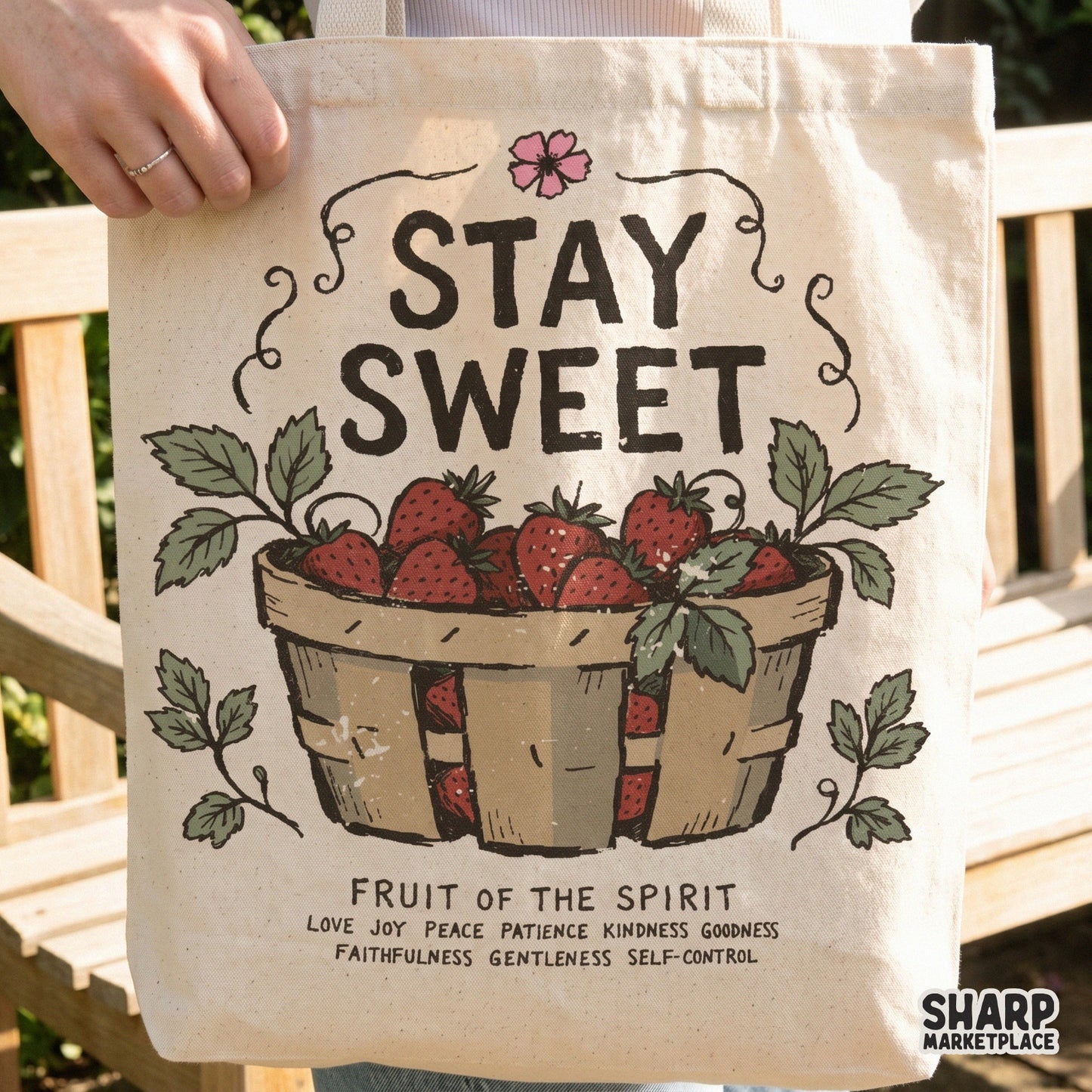 Tote bag mockup featuring a vintage-style strawberry basket illustration with the quote Stay Sweet and a list of spiritual virtues in serif font.