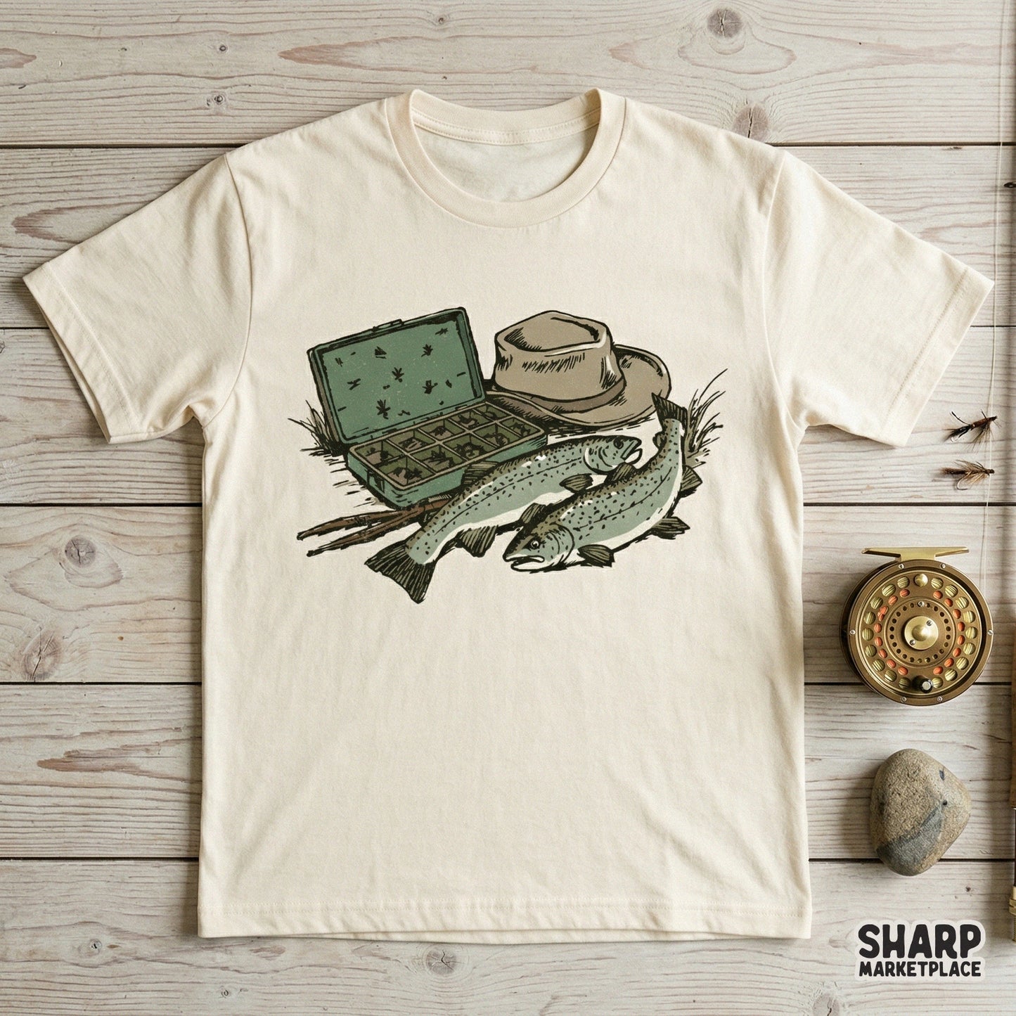 Digital design of trout fishing gear printed on a cream t-shirt, showcasing a fly box, angler hat, and two fish for a rustic outdoor apparel look.