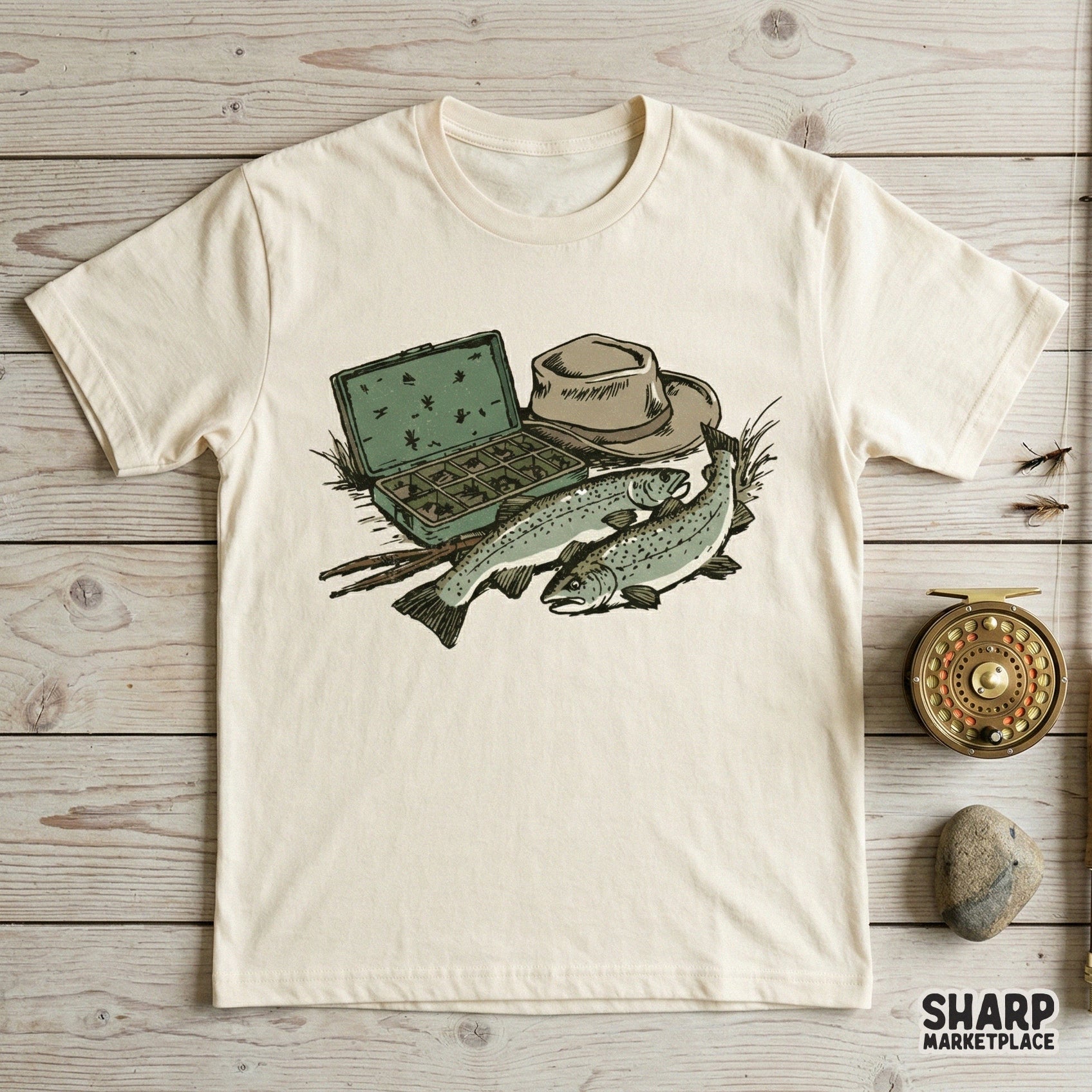 Digital design of trout fishing gear printed on a cream t-shirt, showcasing a fly box, angler hat, and two fish for a rustic outdoor apparel look.
