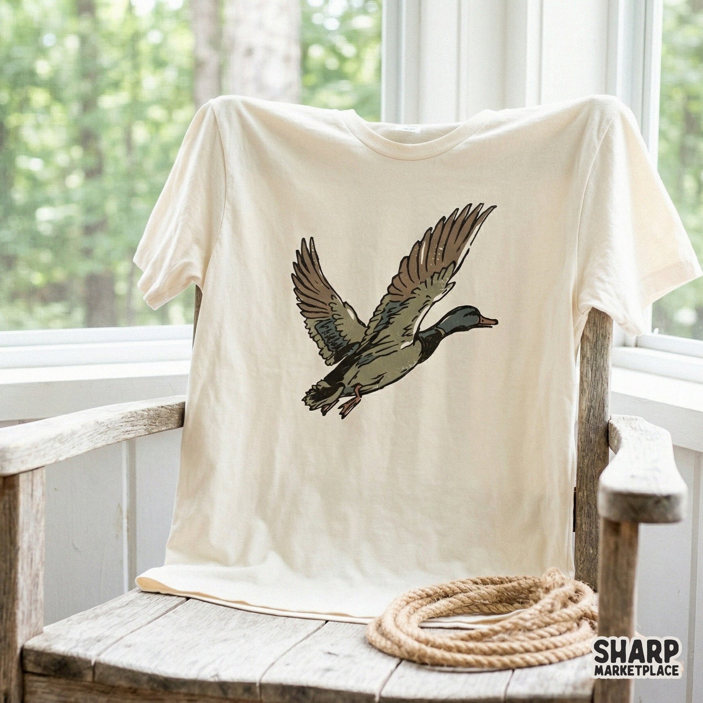 Rustic flying mallard duck design printed on a cream colored t-shirt featuring a hand-drawn block-print aesthetic for outdoor and nature lovers.